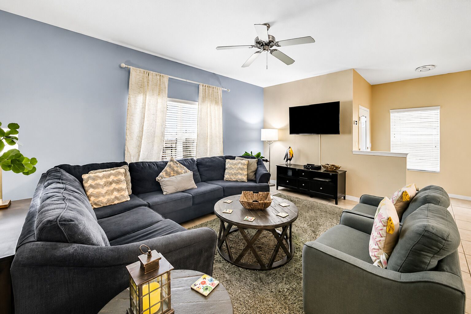 A modern living room with a sectional sofa, a coffee table, and a flat-screen TV mounted on the wall.