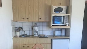A compact kitchen with wooden cabinets, a microwave, a coffee maker, and a dining table set with white cups and saucers. - 200m from ski lifts, 1st floor, balcony, parking, tv, ski locker, 25m², Combloux (Combloux)