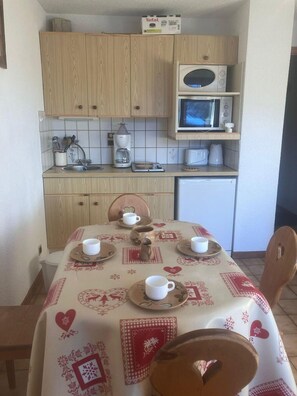 Eine kleine Küche mit Holzausstattung, einer Mikrowelle, einer Kaffeemaschine und einem Esstisch, gedeckt mit weißen Tassen und Untertellern.