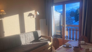 A room with a sofa, a dining table with chairs, and a view of mountains through a window. - 200m from ski lifts, 1st floor, balcony, parking, tv, ski locker, 25m², Combloux (Combloux)