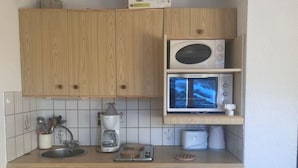 A compact kitchen with wooden cabinets, a microwave, a coffee maker, and a dishwasher. - 200m from ski lifts, 1st floor, balcony, parking, tv, ski locker, 25m², Combloux (Combloux)