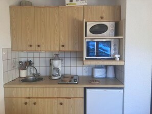 Eine kompakte Küche mit Holzausstattung, einer Mikrowelle, einer Kaffeemaschine und einem Geschirrspüler.