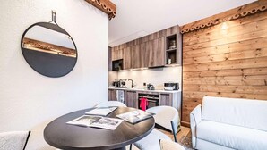 Cozinha moderna com armários de madeira, área de refeições com mesa e cadeiras redondas, e um sofá branco.