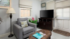 Ein Wohnzimmer mit grauem Sofa, einem Couchtisch mit Buch, einer Stehlampe, einem Fernseher und einem Schrank.