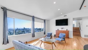 A spacious living room with large windows, a flat-screen TV, and a staircase leading to another level. - 3BD 2BA House Breathtaking Views in Los Feliz Hills (Los Angeles)