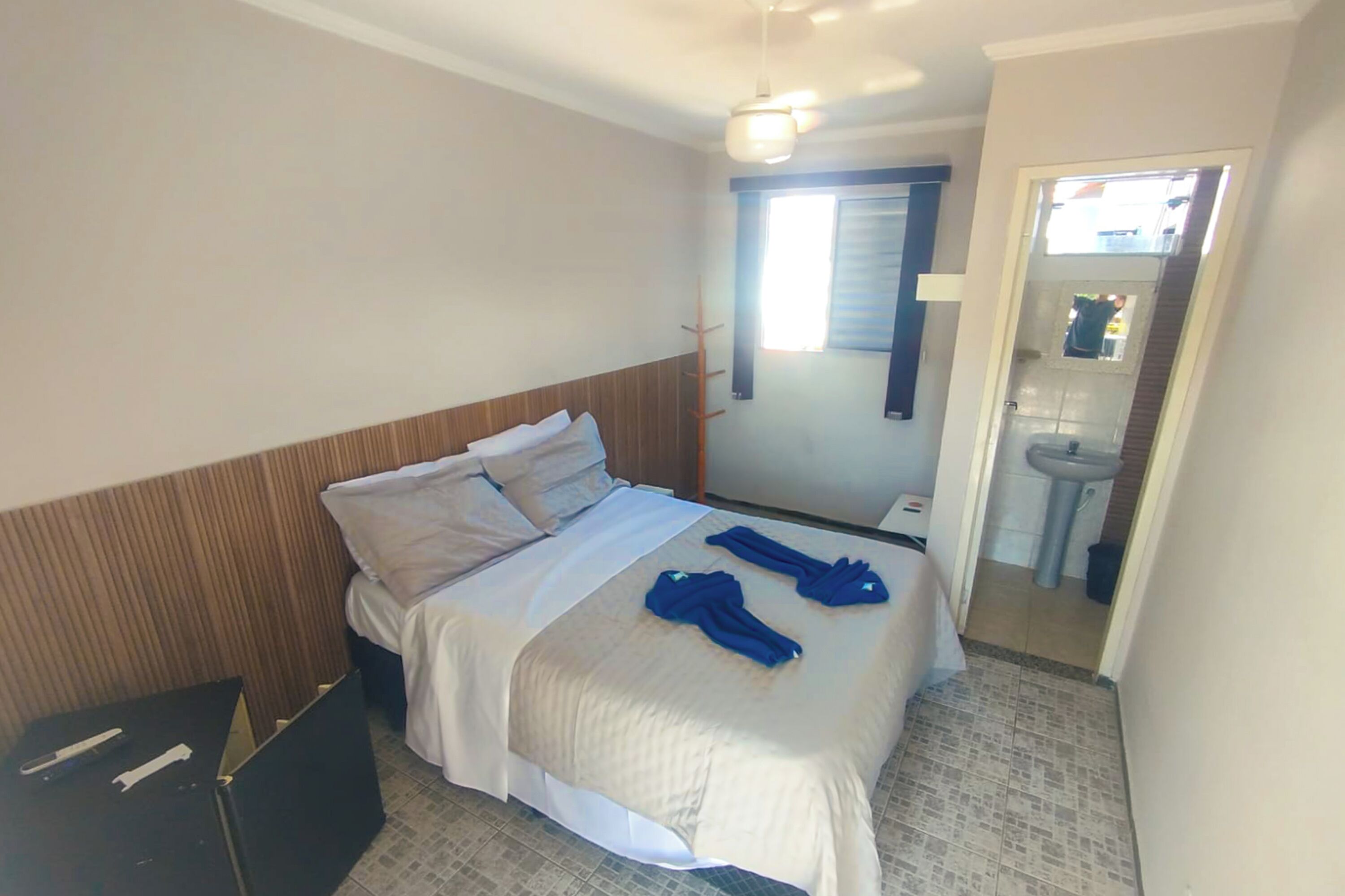Una habitación de hotel con cama, mesita de noche, espejo y baño visible a través de una puerta abierta.