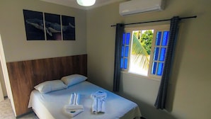 A hotel room with a bed, a headboard, a window with blue curtains, and wall-mounted air conditioning.