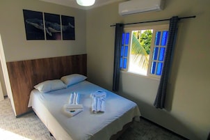 Habitación de hotel con una cama, cabecero, ventana con cortinas azules y aire acondicionado instalado en la pared.