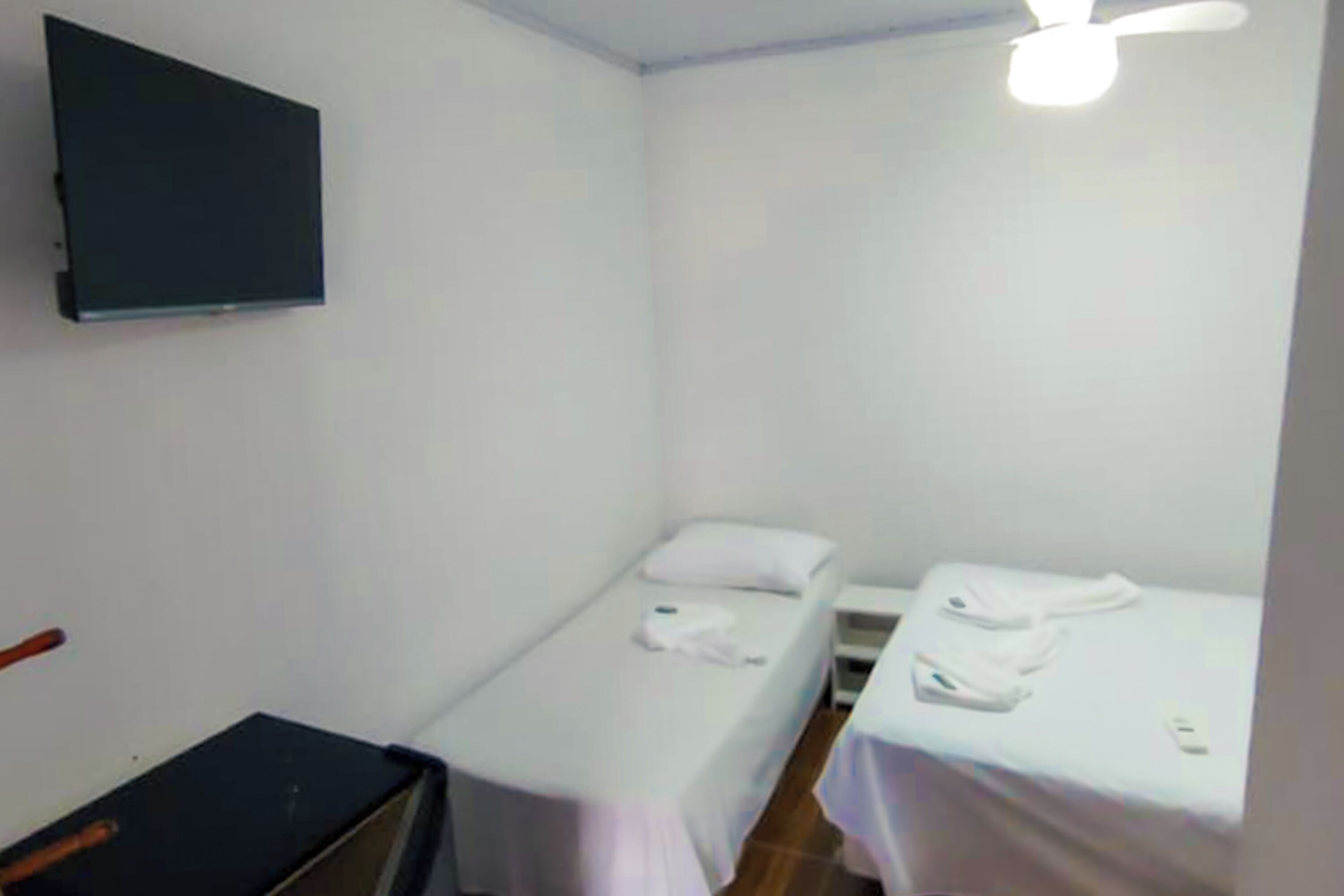 Une petite pièce avec deux lits, un téléviseur fixé au mur et un ventilateur de plafond.