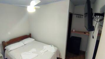 A bedroom with a bed, a ceiling fan, a TV mounted on the wall, and a small shelf with a cup.