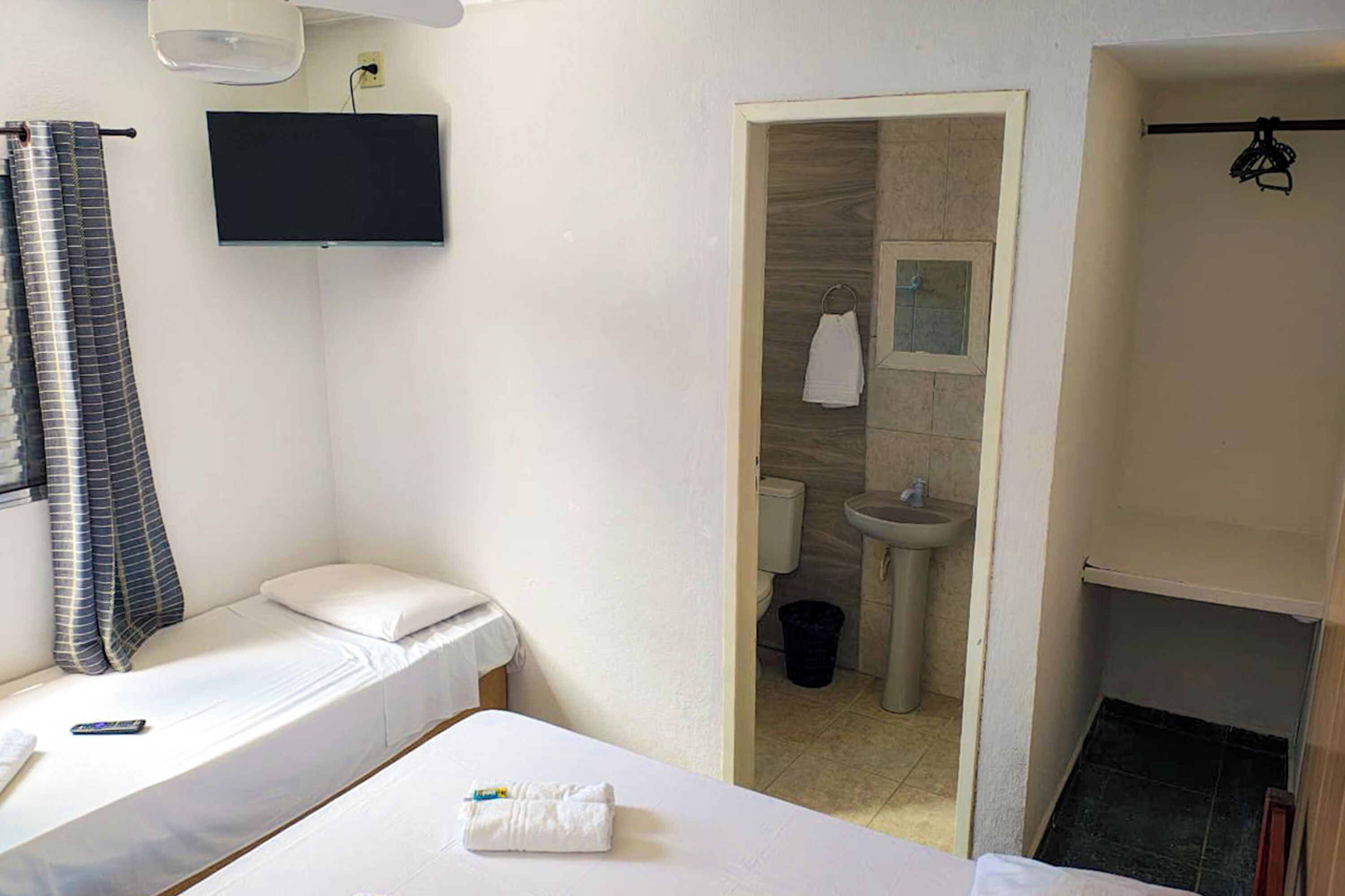 Een hotelkamer met een bed, een aan de muur bevestigde televisie, een badkamer met een wastafel en spiegel, en een handdoek op het bed.