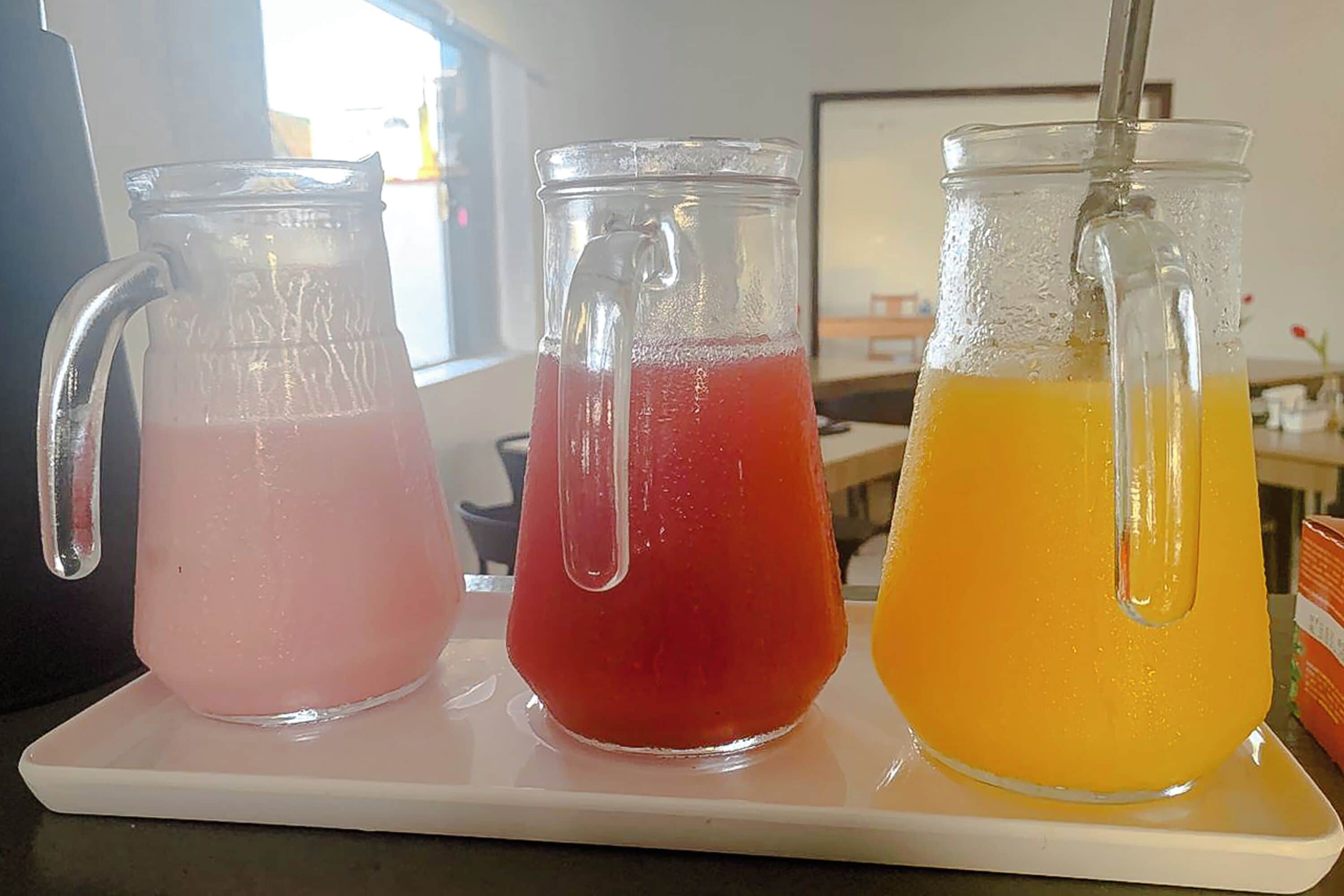 Tres jarras de vidrio con bebidas de diferentes colores sobre una bandeja blanca.
