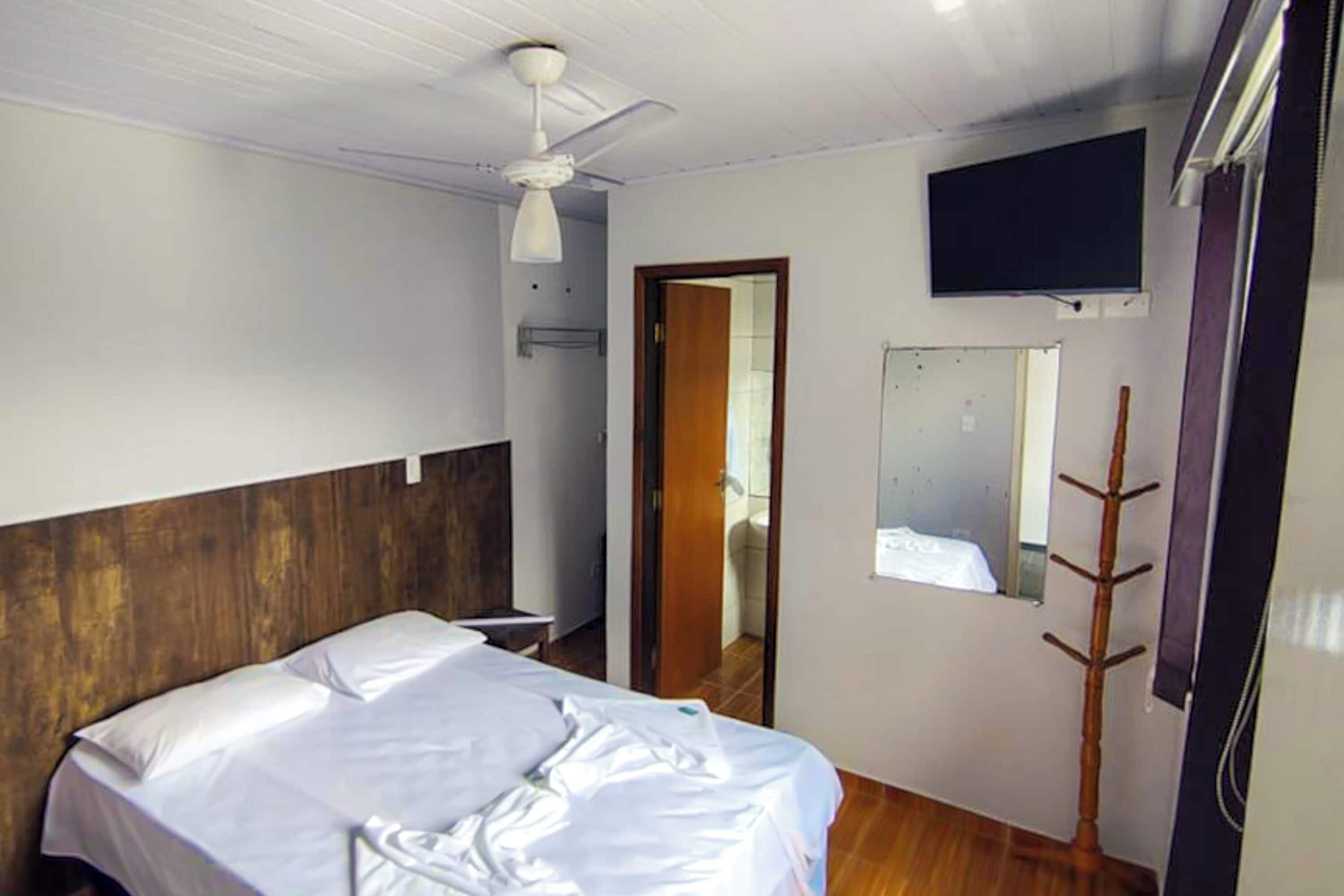 A bedroom with a bed, a ceiling fan, a TV mounted on the wall, and a wooden coat rack.