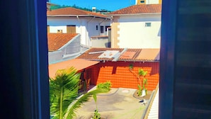 A view from a window of a residential area with a red-roofed building, a paved courtyard, and a palm tree.