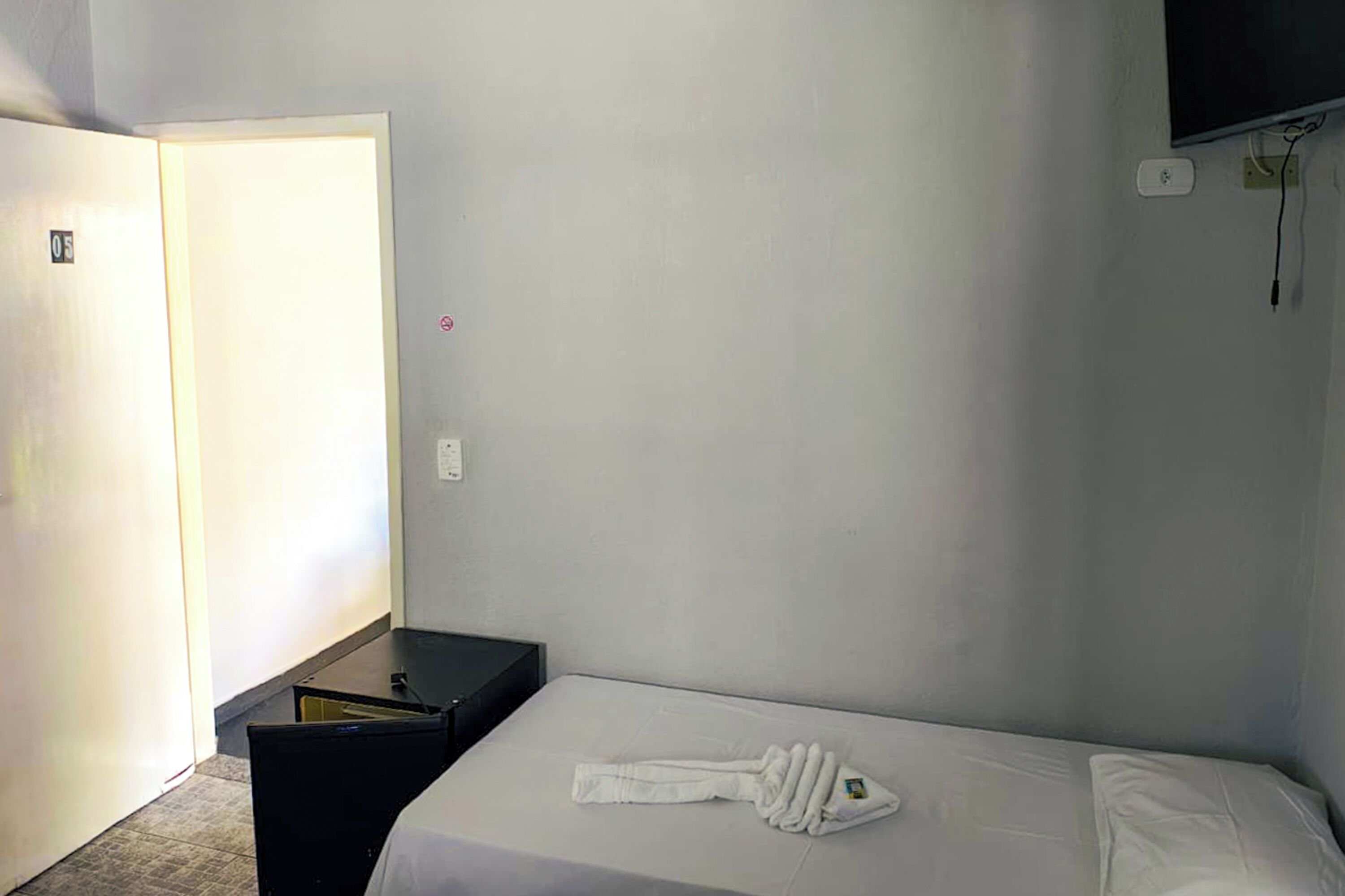 Ein Hotelzimmer mit Bett, einem kleinen Tisch, einem an der Wand befestigten Fernseher und einer Tür mit einer Nummer.