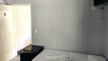Ein Hotelzimmer mit Bett, einem kleinen Tisch, einem an der Wand befestigten Fernseher und einer Tür mit einer Nummer.
