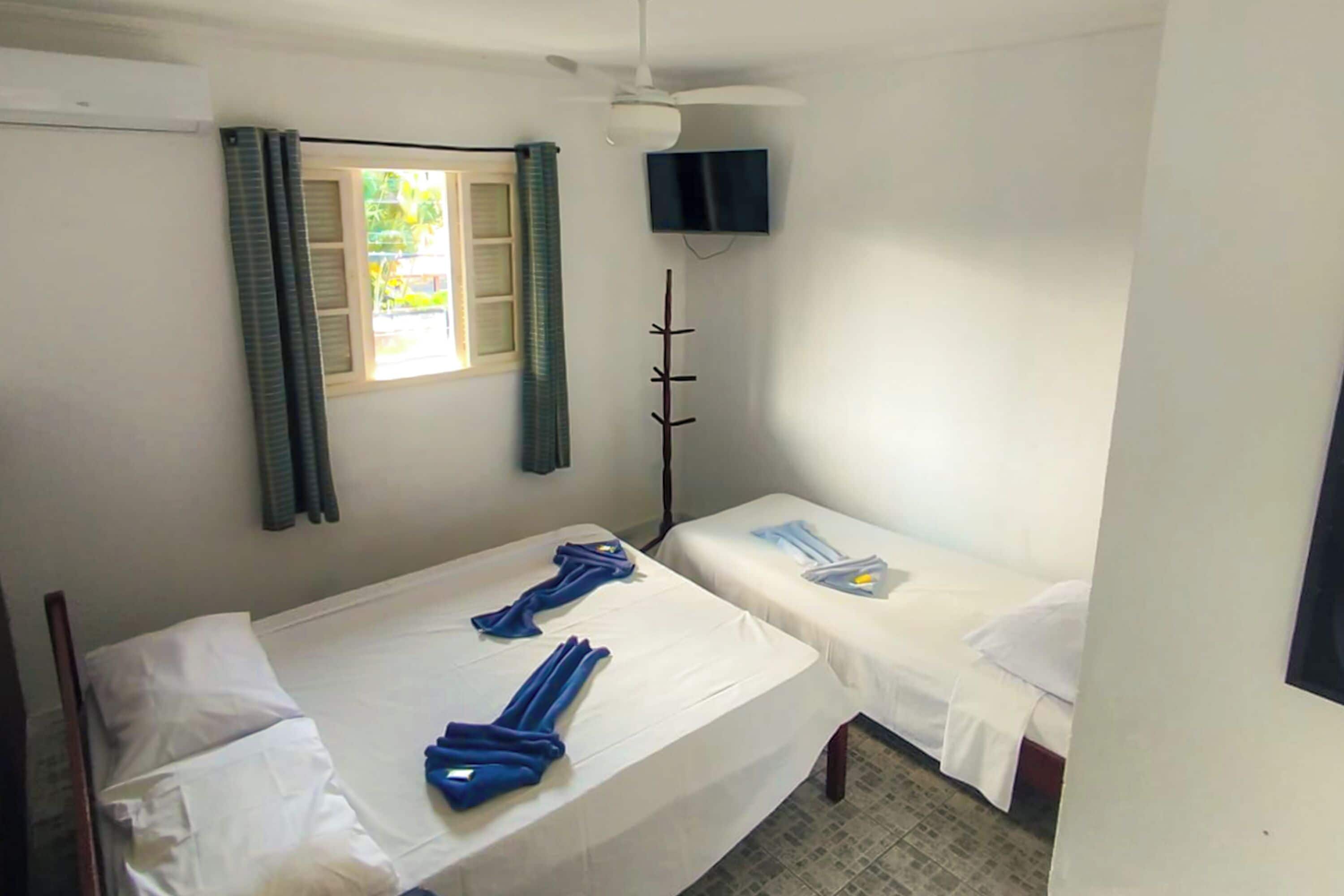 A room with two beds, a ceiling fan, a TV, and a window with curtains.