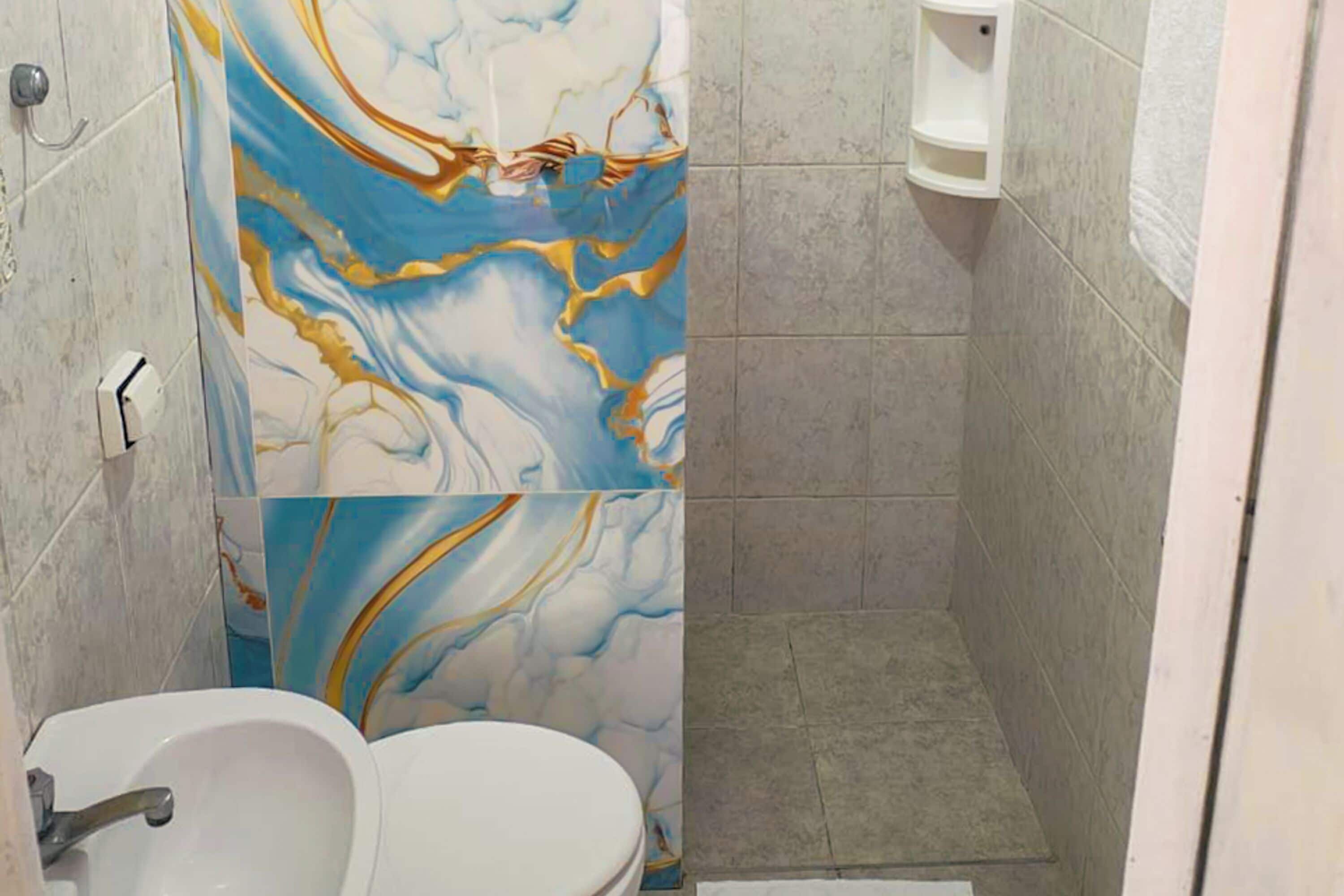 A bathroom with a marble shower wall, a white sink, and a small shelf.