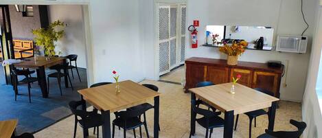 Un comedor con mesas y sillas, un extintor, un microondas y un mueble con un jarrón de flores.