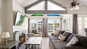A spacious living room with a fireplace, a ceiling fan, and a large window with curtains. - Perfect Newport Beach Location With Balcony & Spa (Newport Beach)