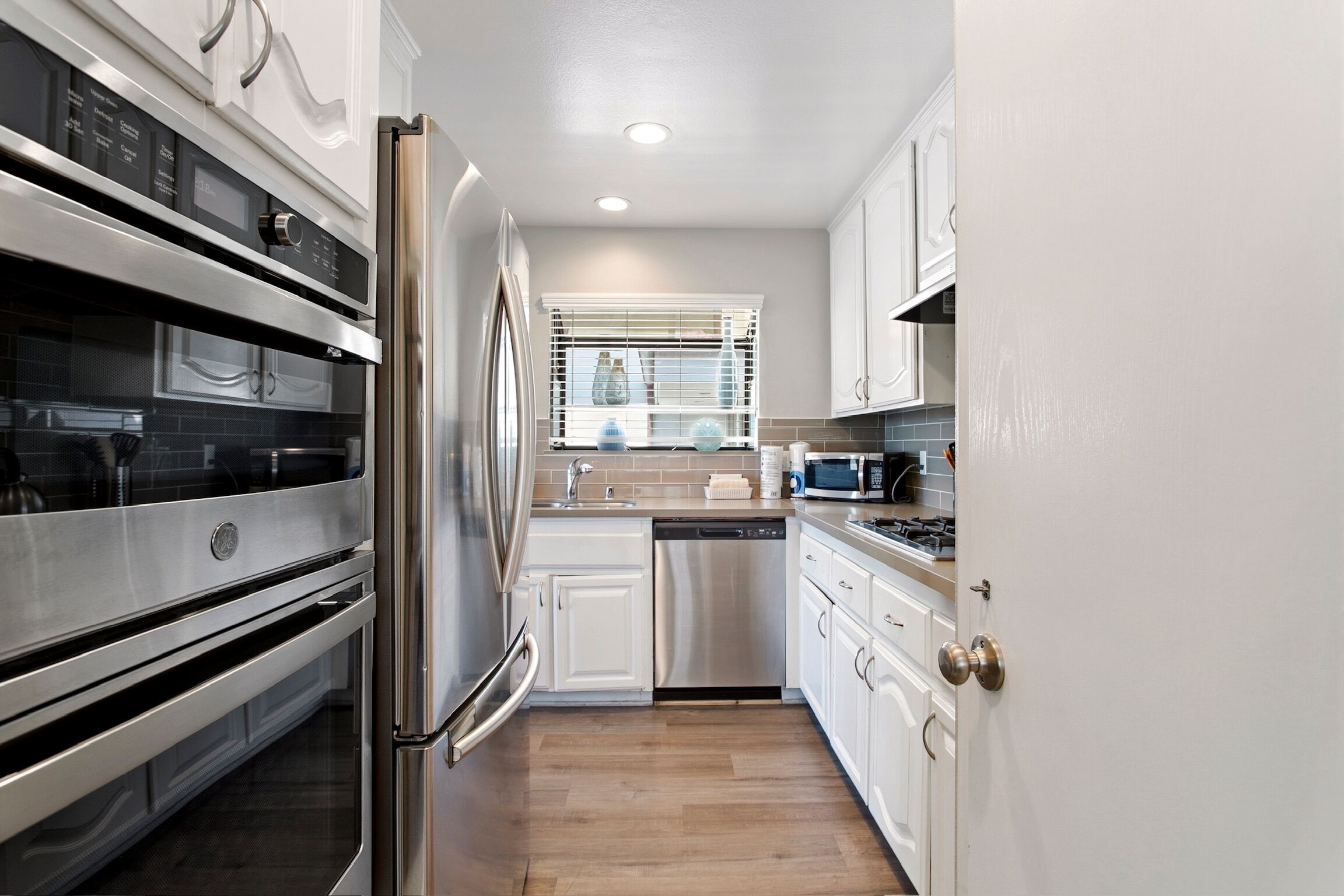 A modern kitchen with stainless steel appliances, white cabinetry, and a window with blinds.