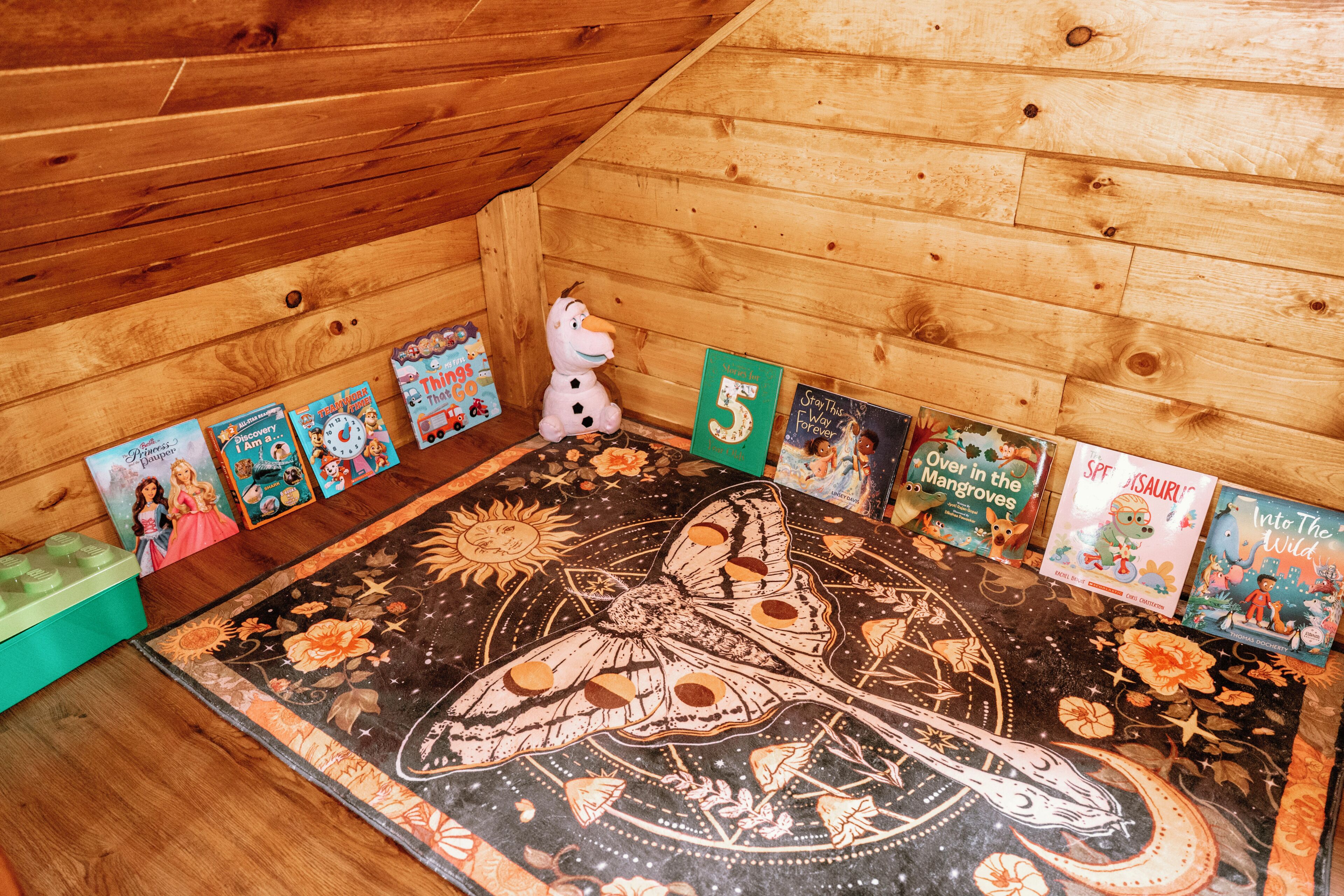 A wooden room with a large butterfly illustration on the floor, surrounded by children's books.