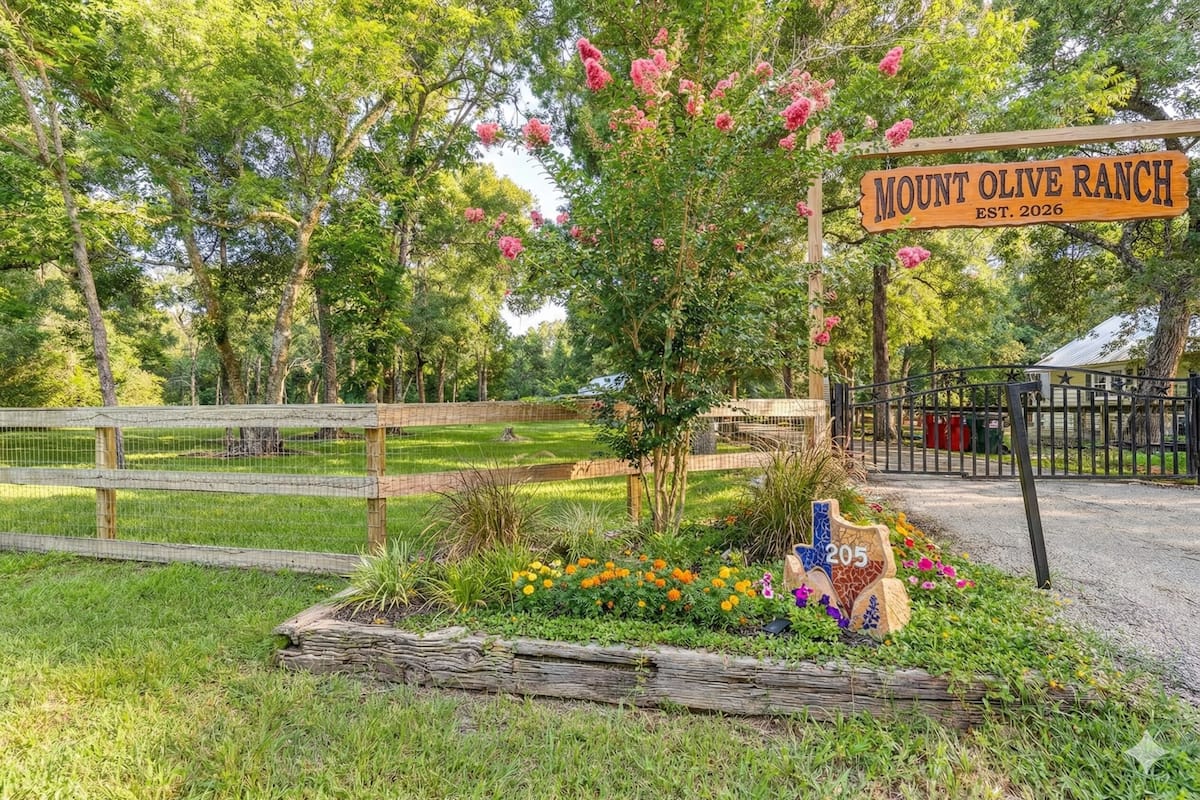 A ranch sign, a wooden fence, and a flower bed with a variety of flowers.