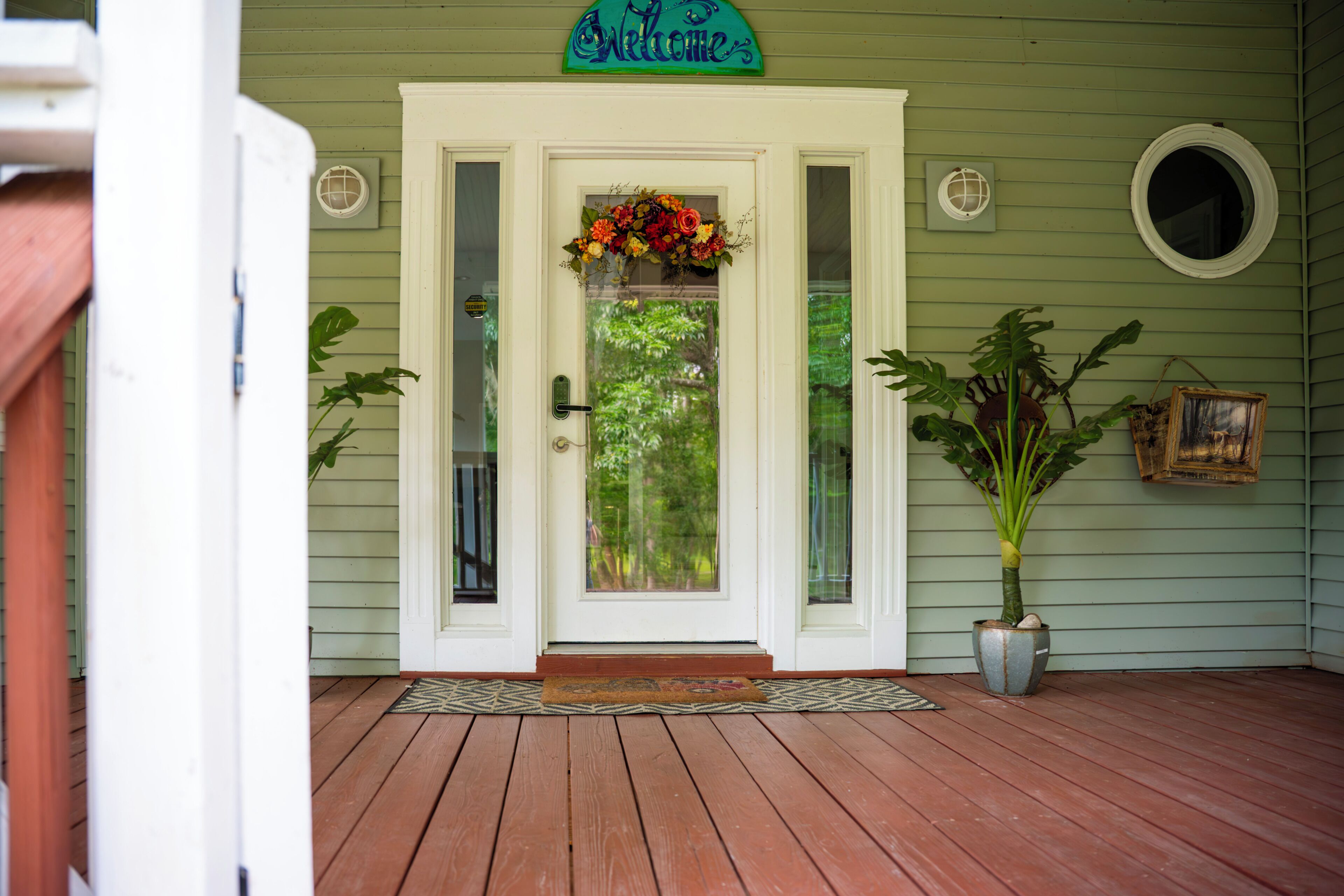 A front door with a welcome sign, a flower arrangement, and a potted plant.
