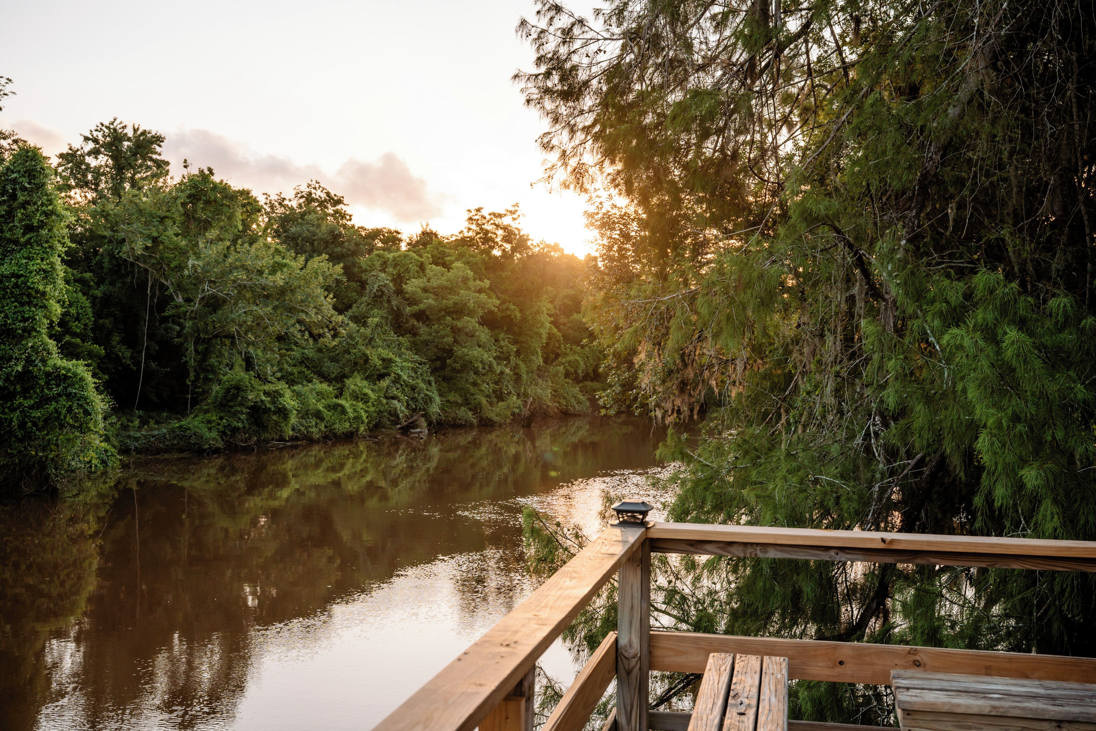 A wooden deck overlooking a calm river with dense forest on one side.