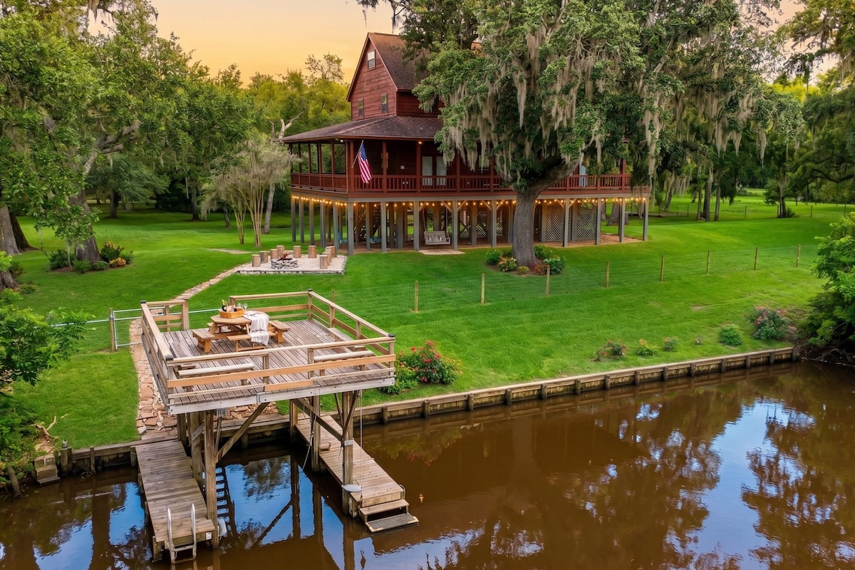 A wooden house with a porch, a dock, and a lawn.