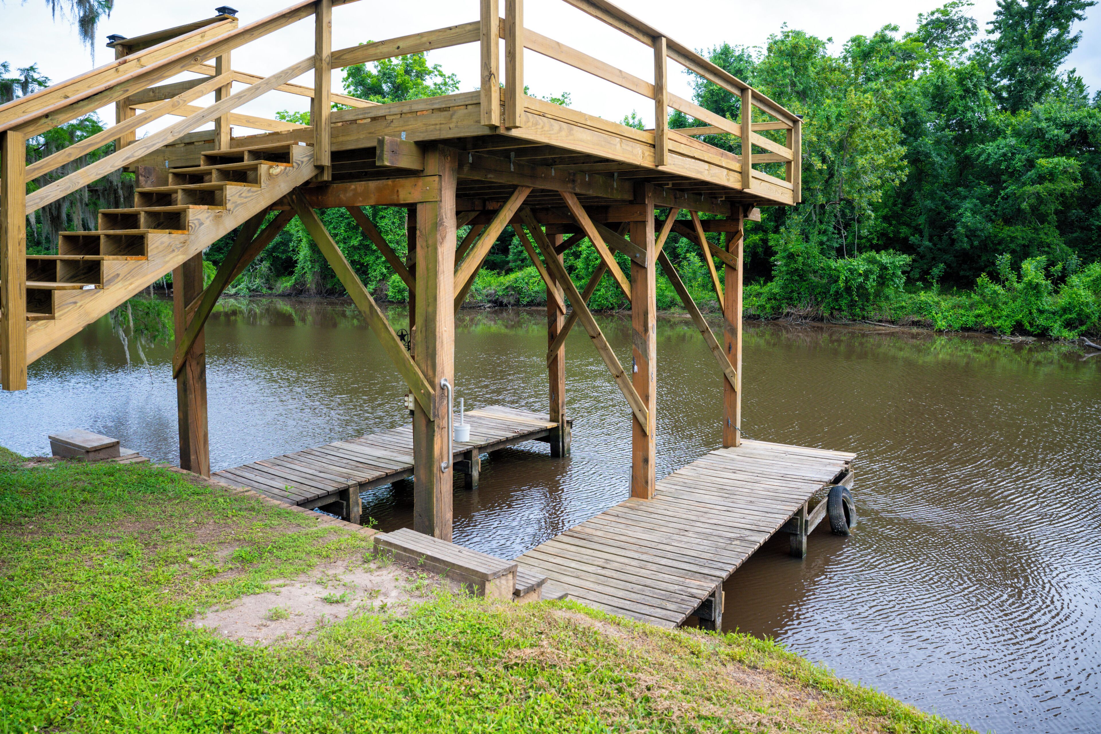 Eine Holzbrücke mit Treppen, die über ein Gewässer führen, umgeben von Grün.