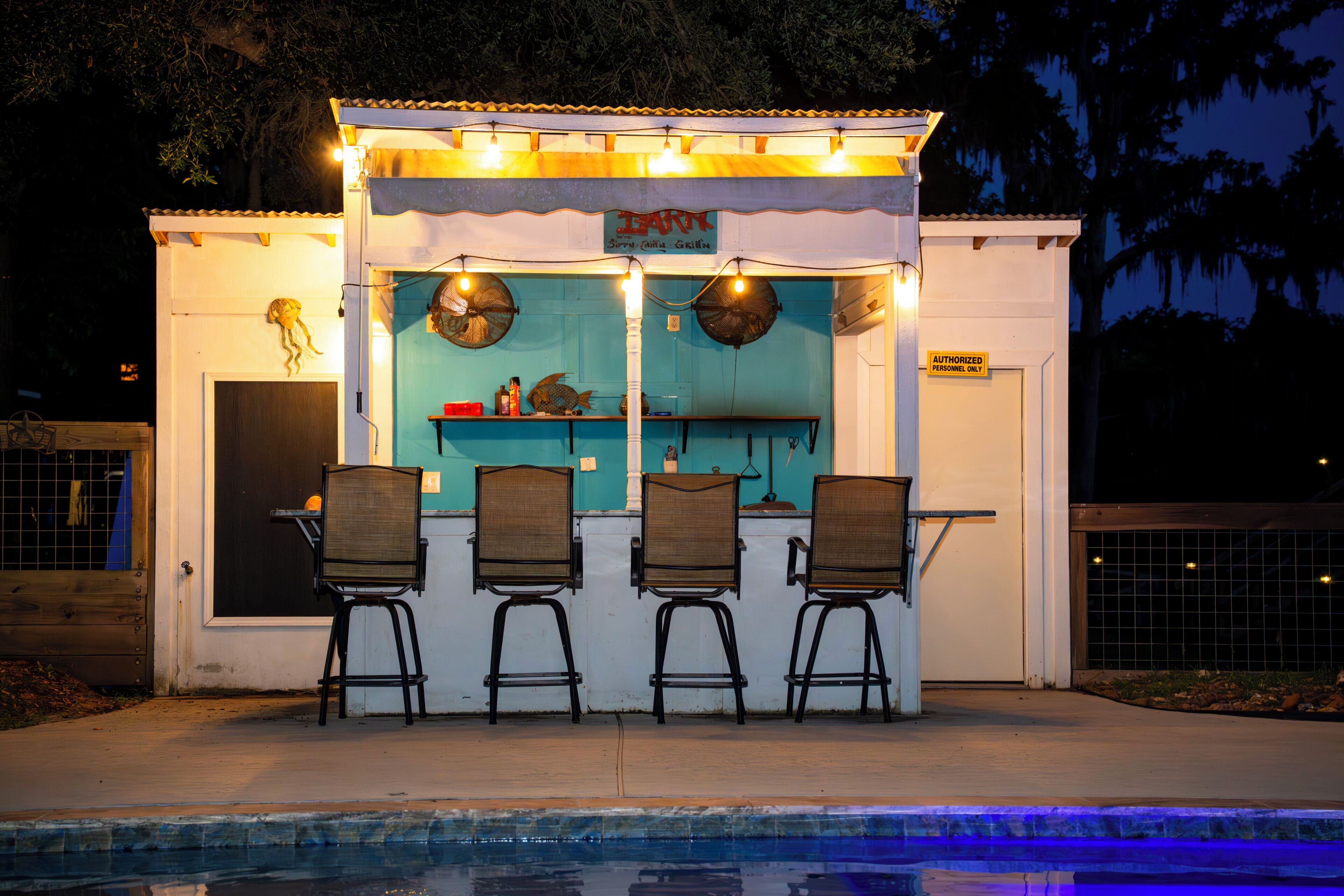 A small outdoor bar with three chairs and a pool in the foreground.