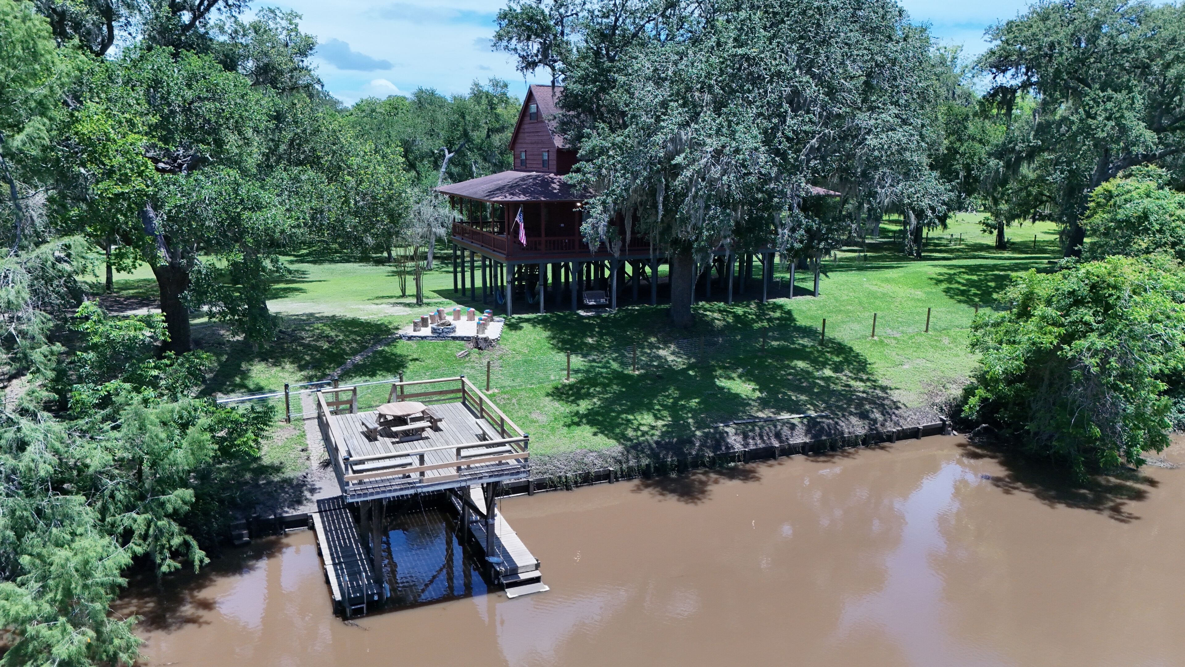 A lodge with a covered deck, a small dock, and a grassy area with a fire pit.