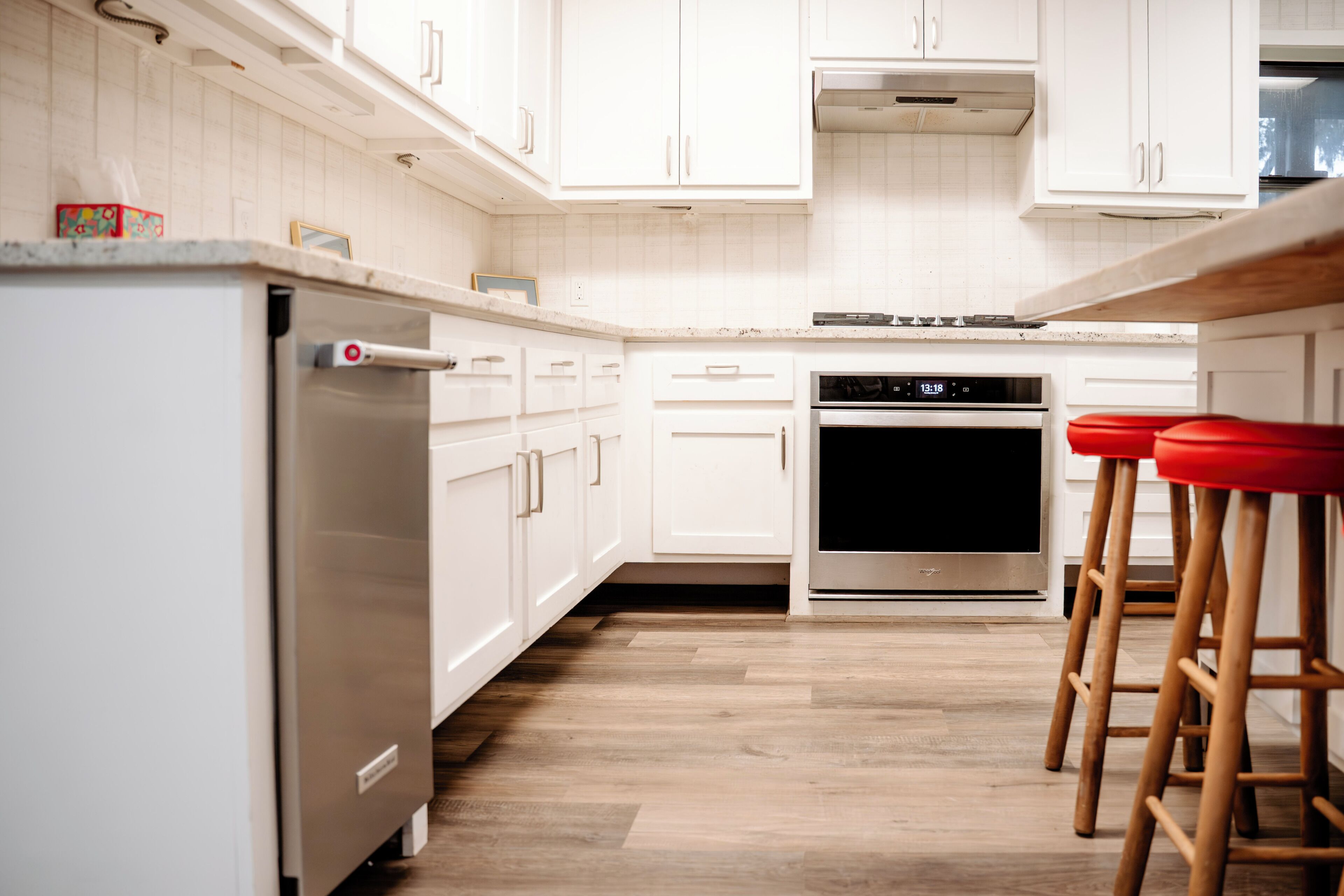Una cocina moderna con armarios blancos, electrodomésticos de acero inoxidable y taburetes de madera.