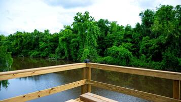 A wooden deck with a bench, overlooking a calm body of water and dense green foliage.