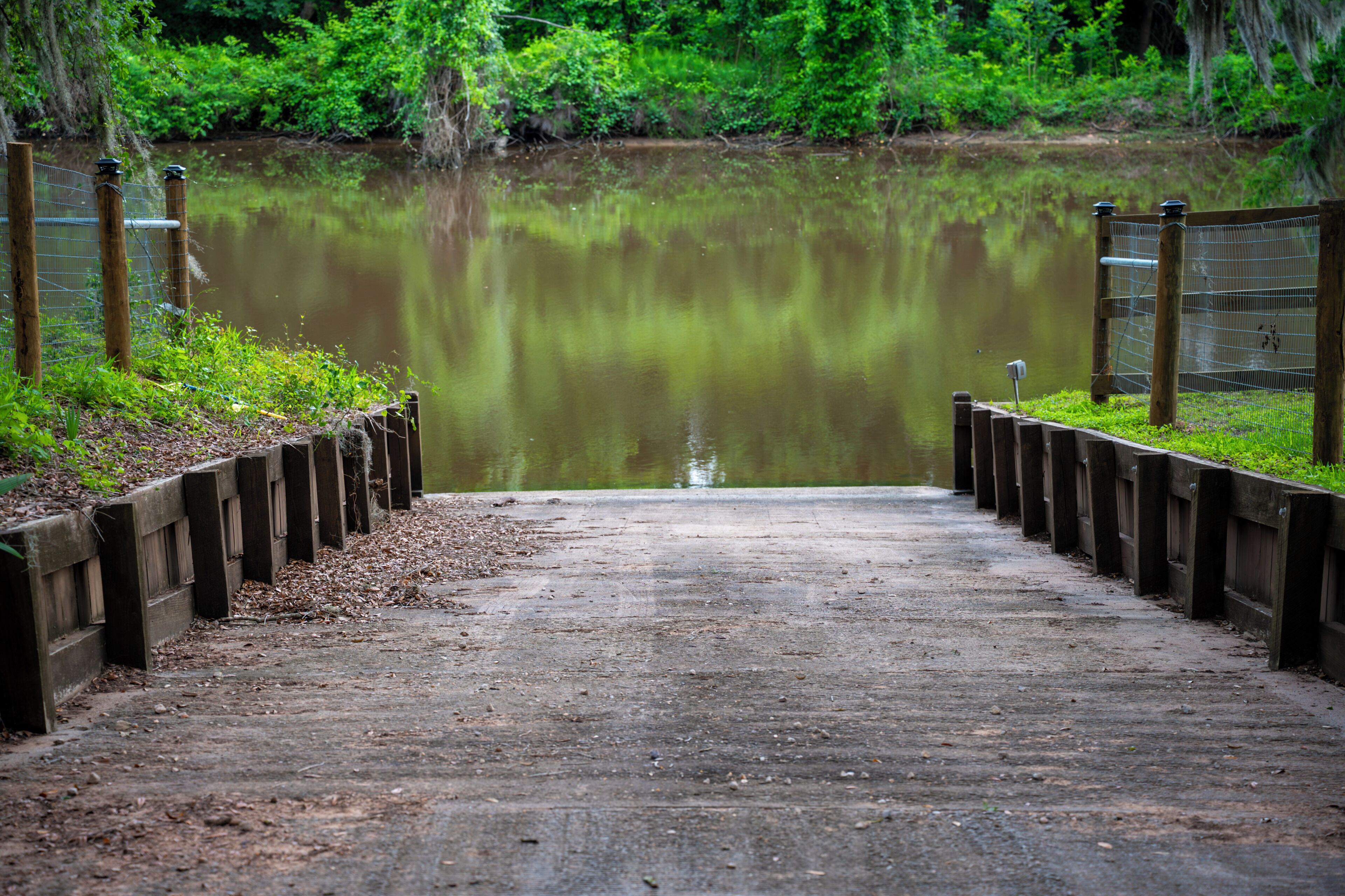 Un pont en béton qui mène à une étendue d’eau paisible, avec une clôture en bois de chaque côté.
