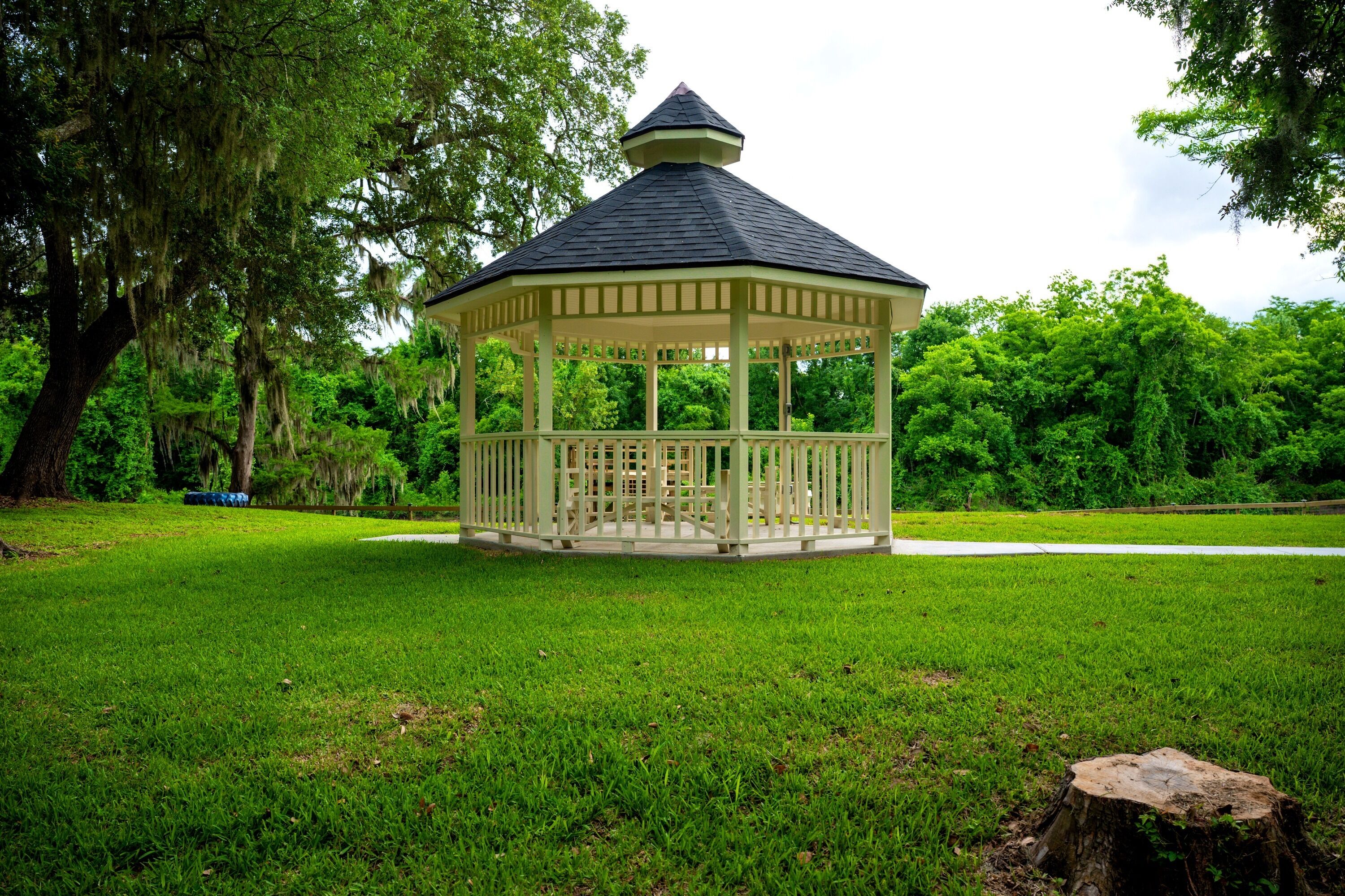 A gazebo with a conical roof, surrounded by lush greenery and trees.