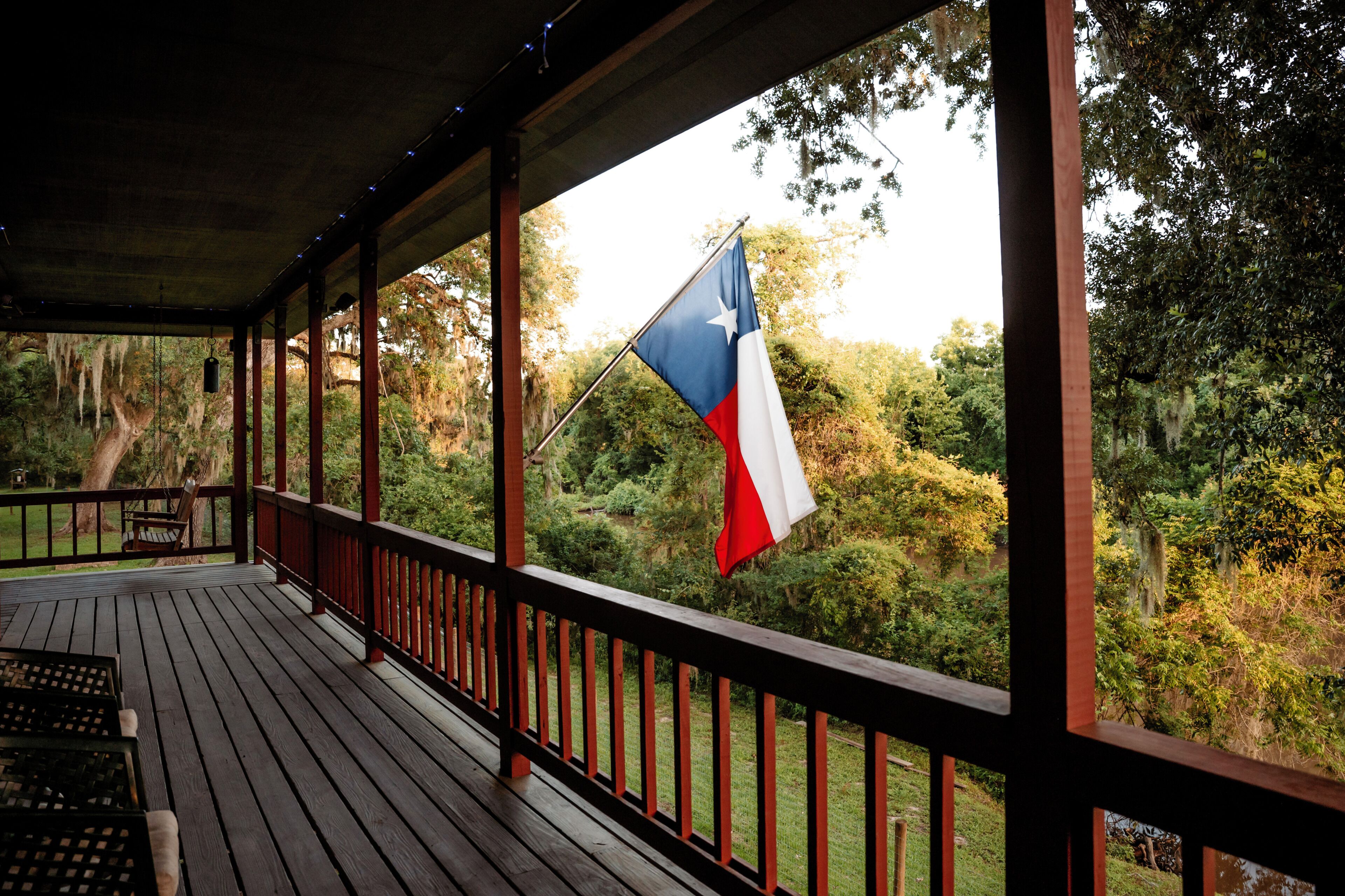 A wooden deck with a Texas flag, surrounded by greenery.