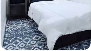 Quarto pequeno com uma cama de solteiro, janela, mesa de cabeceira e chão estampado.