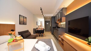 A modern hotel room with a bed, a dining area, a kitchen, and a TV. - Studio em frente a UFSC e HU - 502A (Florianópolis)