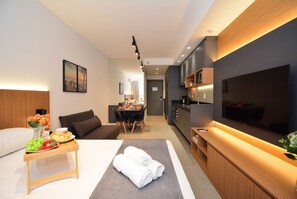 Una habitación de hotel moderna con cama, zona de comedor, cocina y televisor.