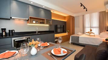 A modern hotel room with a kitchenette, a dining area, a bed, and a TV.
