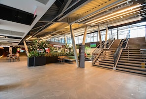 A spacious indoor area with a staircase, seating areas, and a sign for 'BENVENUTO.' - Studio em frente a UFSC e HU - 502A (Florianópolis)