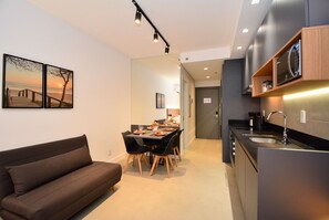 A modern kitchen with a built-in microwave, a dining area with a table and chairs, and a sofa. - Studio em frente a UFSC e HU - 502A (Florianópolis)