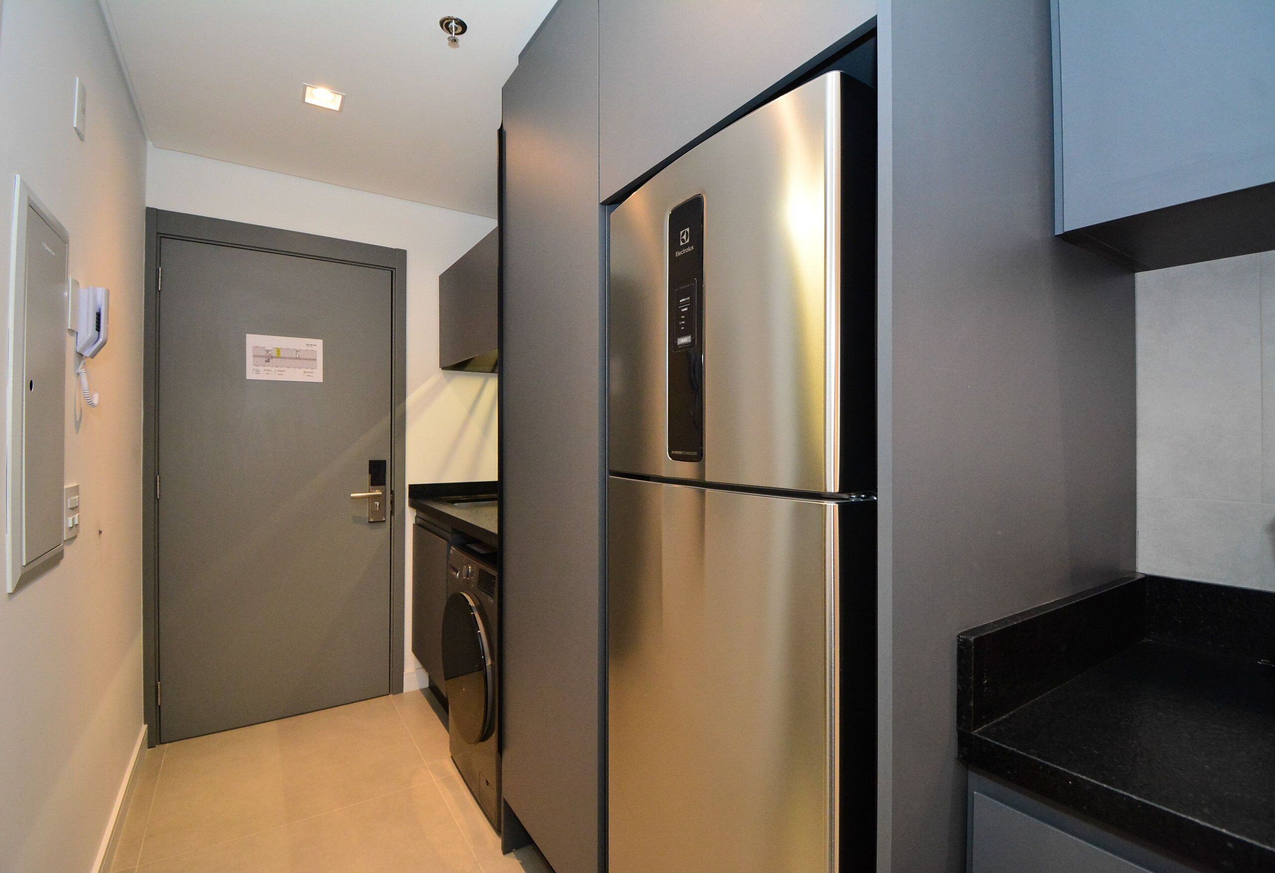 Una cocina compacta con un refrigerador de acero inoxidable, una lavadora y una puerta con un aviso.