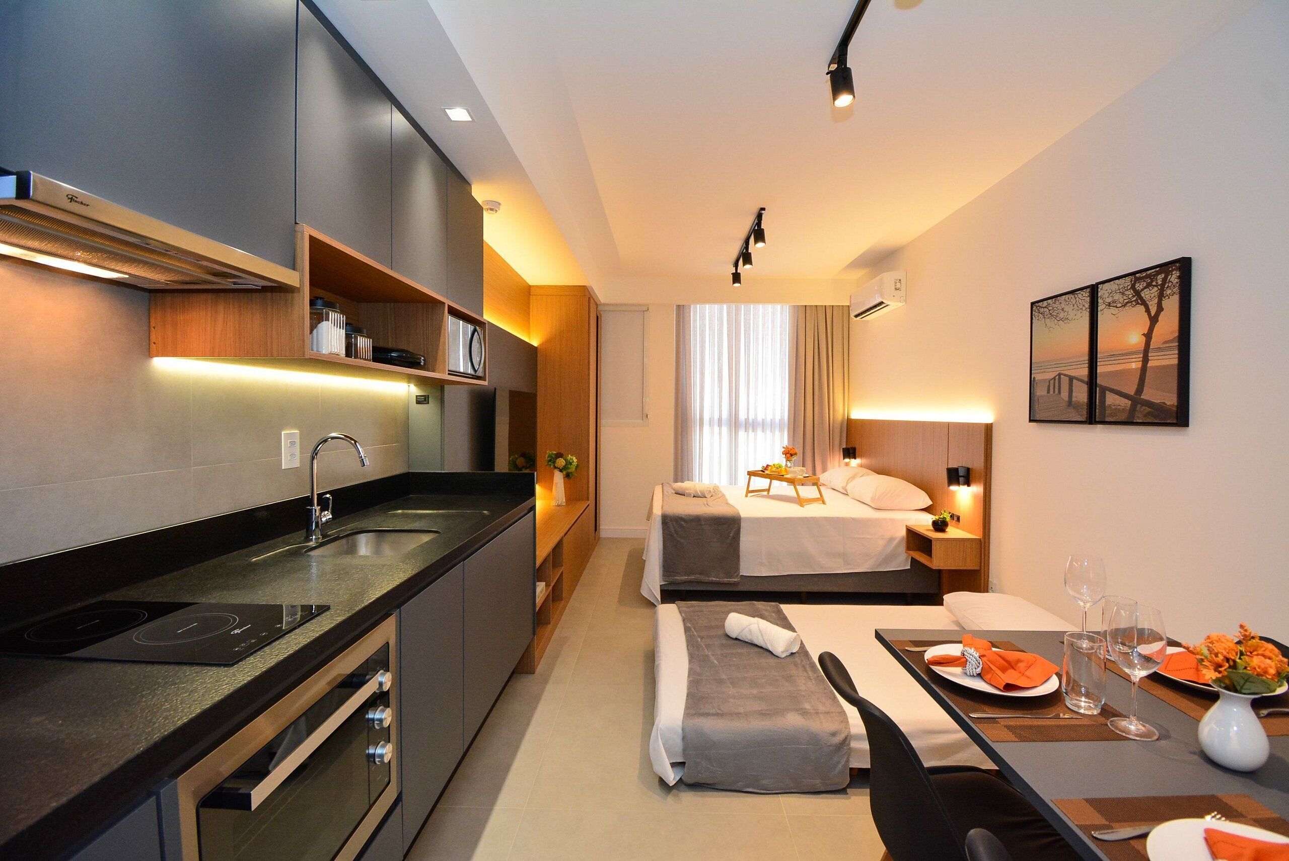 A modern hotel room with a kitchenette, a bed with a view, and a dining area.