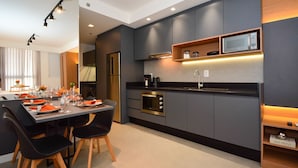 Une cuisine moderne dotée d’appareils électroménagers intégrés, un coin repas avec une table dressée pour deux personnes, et une petite étagère sur laquelle se trouve un four à micro-ondes.