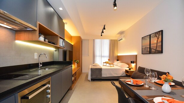 A modern hotel room with a kitchenette, a dining area, a bed, and a view of the outdoors. - Studio em frente a UFSC e HU - 502A (Florianópolis)