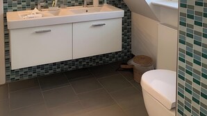 Un bagno con un lavandino bianco, due specchi, uno schienale piastrellato, un WC bianco e una trave in legno al soffitto.