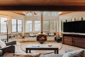 A cozy living room with a wood-burning stove, comfortable seating, and large windows. - Golden Hour | Jacuzzi, Sauna, Pool, Tennis, Gated! (Big Bear Lake)